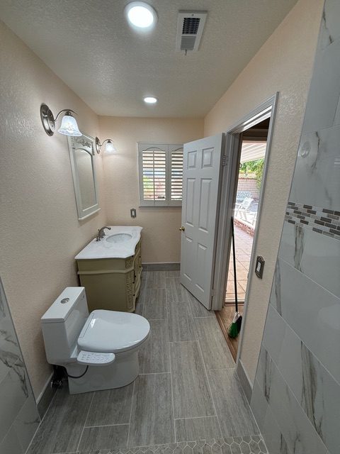 Bathroom interior featuring a white toilet, a light-colored vanity with a sink, modern lighting fixtures, and a window with shutters, showcasing a recently remodeled space.