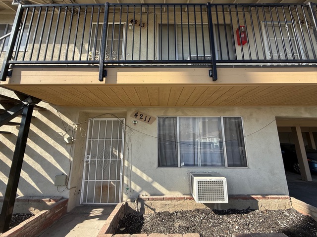 Front view of a residential building with a balcony, featuring unit numbers 4211 and 4213, a gated entrance, and an air conditioning unit below the window, illustrating typical housing in Riverside and San Bernardino counties.