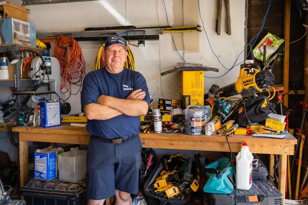 Man standing with arms crossed in a cluttered garage filled with tools and construction equipment, representing BPP Construction's expertise in home inspections and repairs.